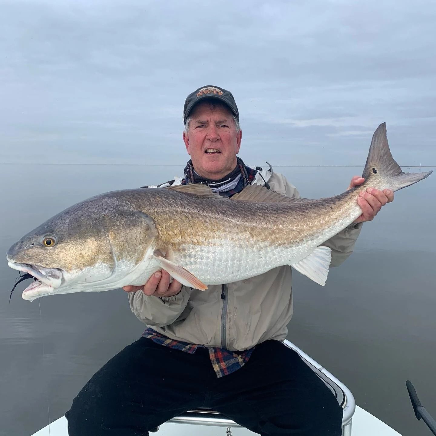 Man holding a large redfish on a boat. Cloudy day.