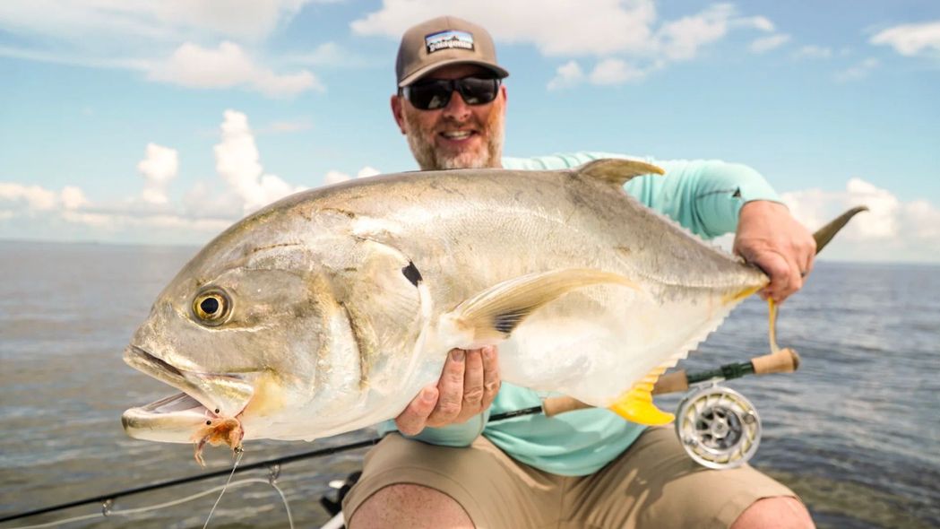 Man holding a large fish caught fly fishing on a boat, sunny day.