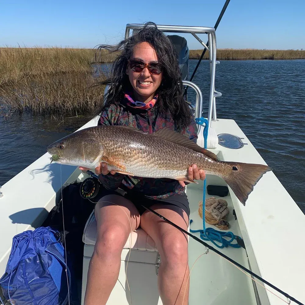 Woman on a boat holding a large redfish; sunny day, coastal setting.