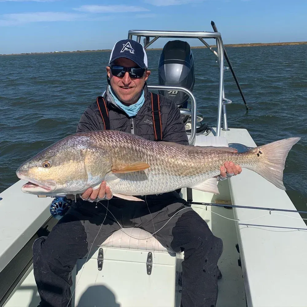 Man in a boat holds a large reddish fish; on the water; sunny day.
