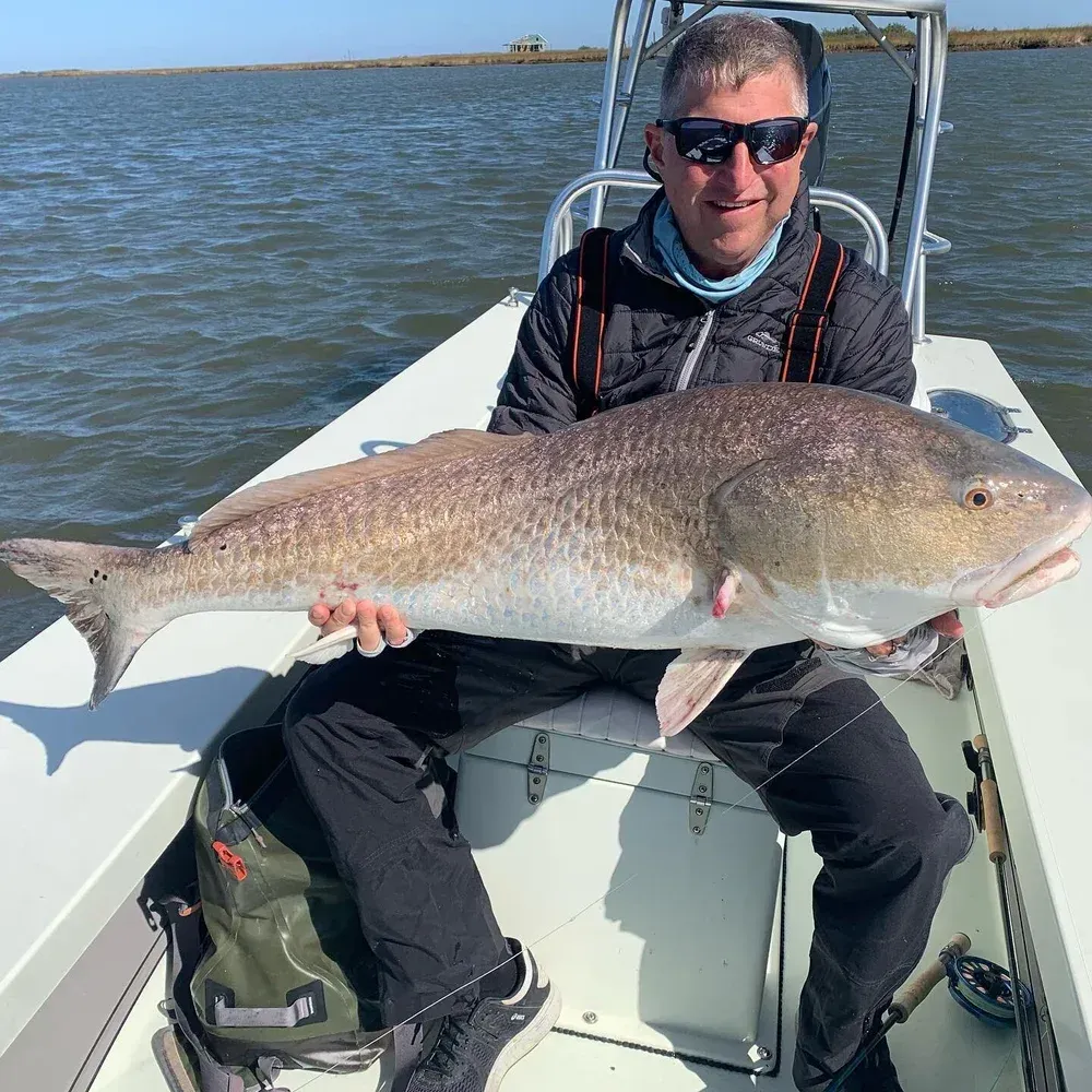 Man in boat holds large redfish; blue water and sky.