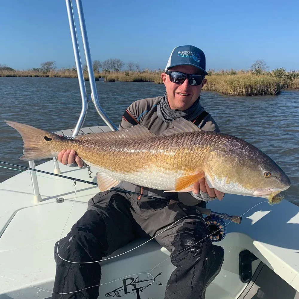 Man in boat holding large redfish. Blue water and sky, coastal setting.
