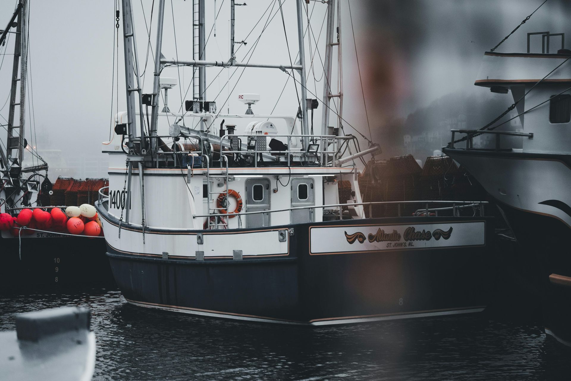White and blue fishing boat docked at harbor, cloudy sky, red buoys visible.