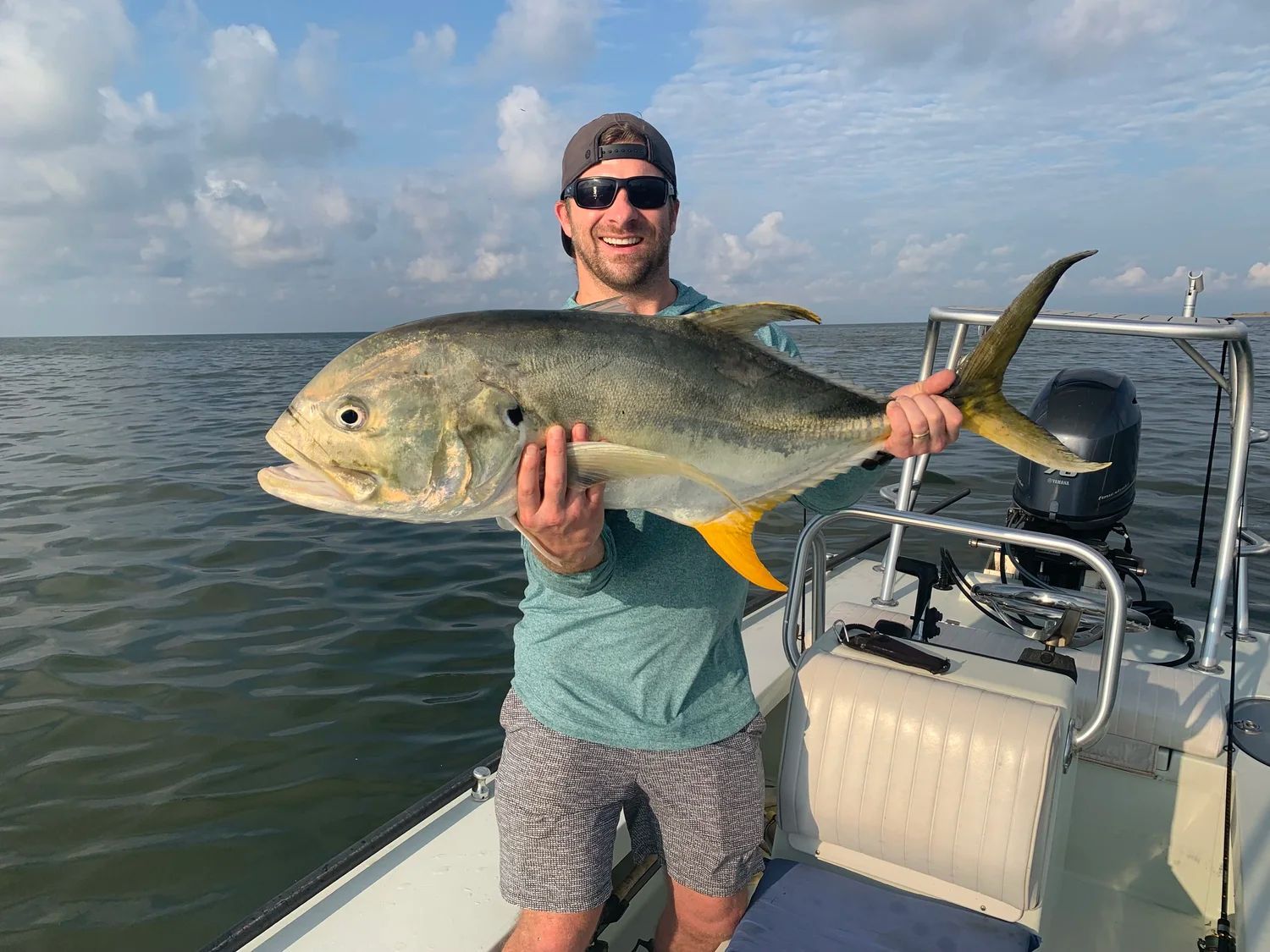 Man on a boat holding a large, yellowtail jack fish. Cloudy sky and ocean.