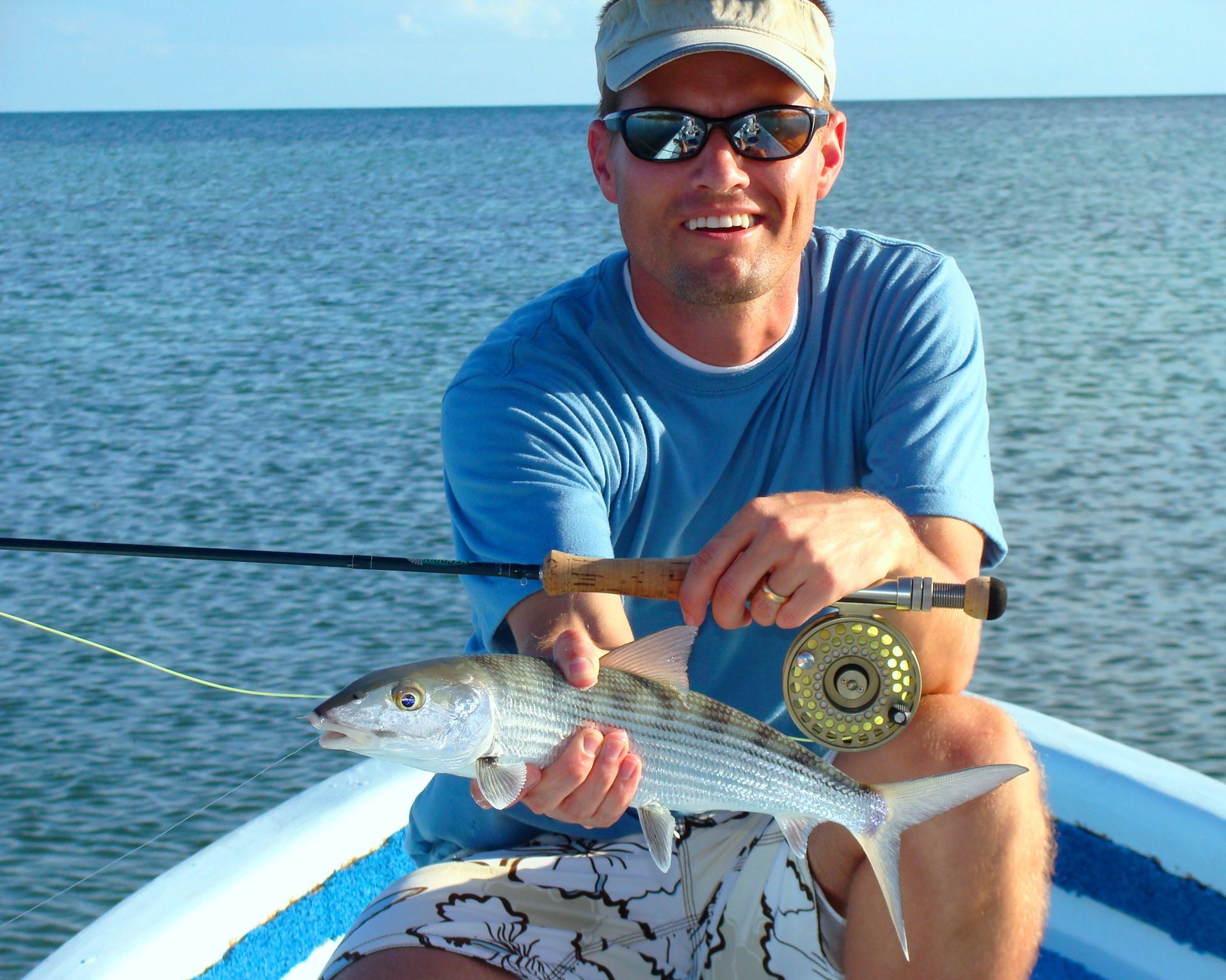 Man in boat holding a fish he caught while fly fishing on the ocean.