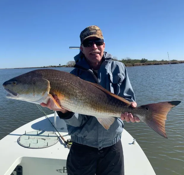 Man on a boat holds a large redfish. Cloudy sky, calm water.