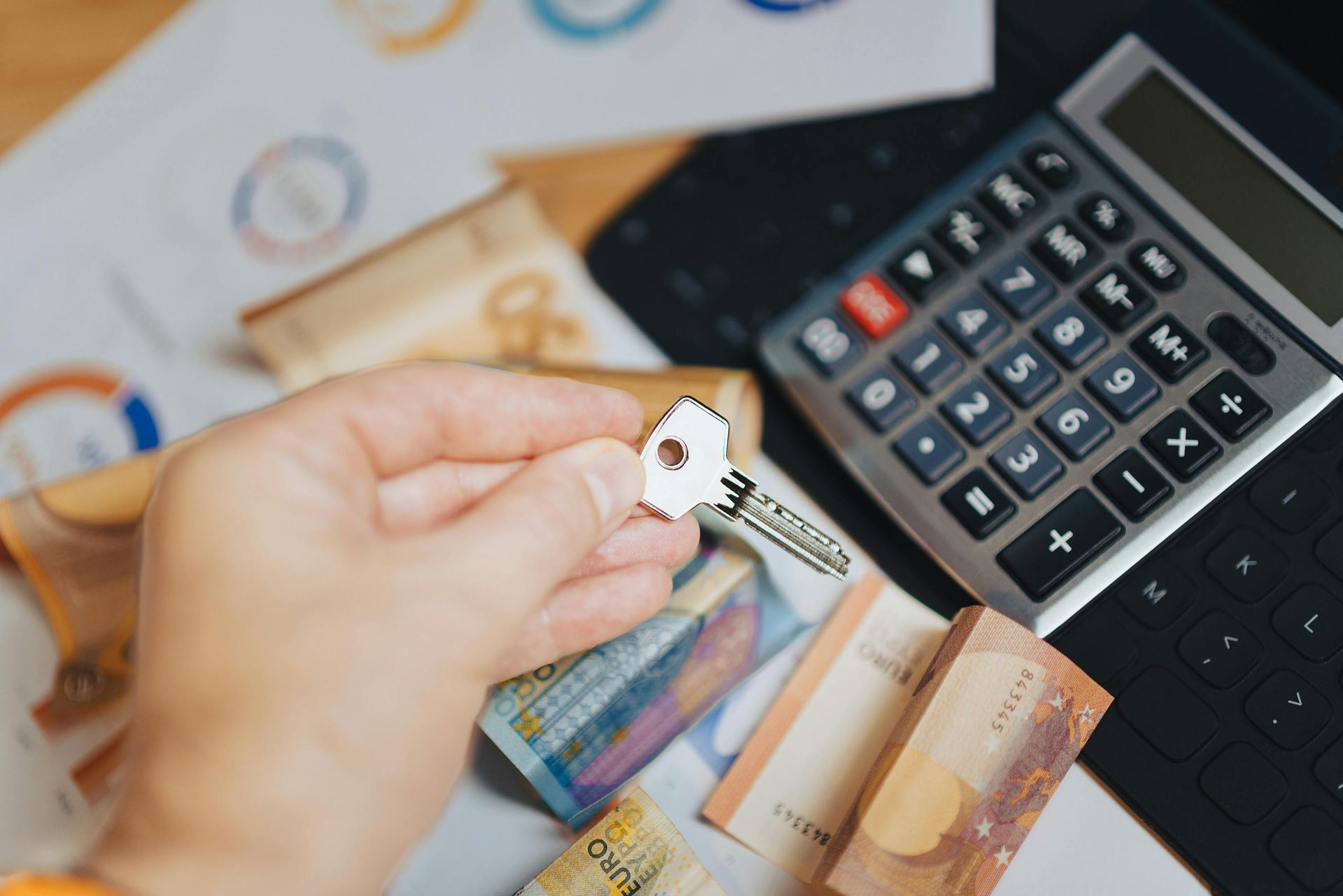 Person holding a key over cash, calculator, and documents on a dark surface, suggesting financial planning.