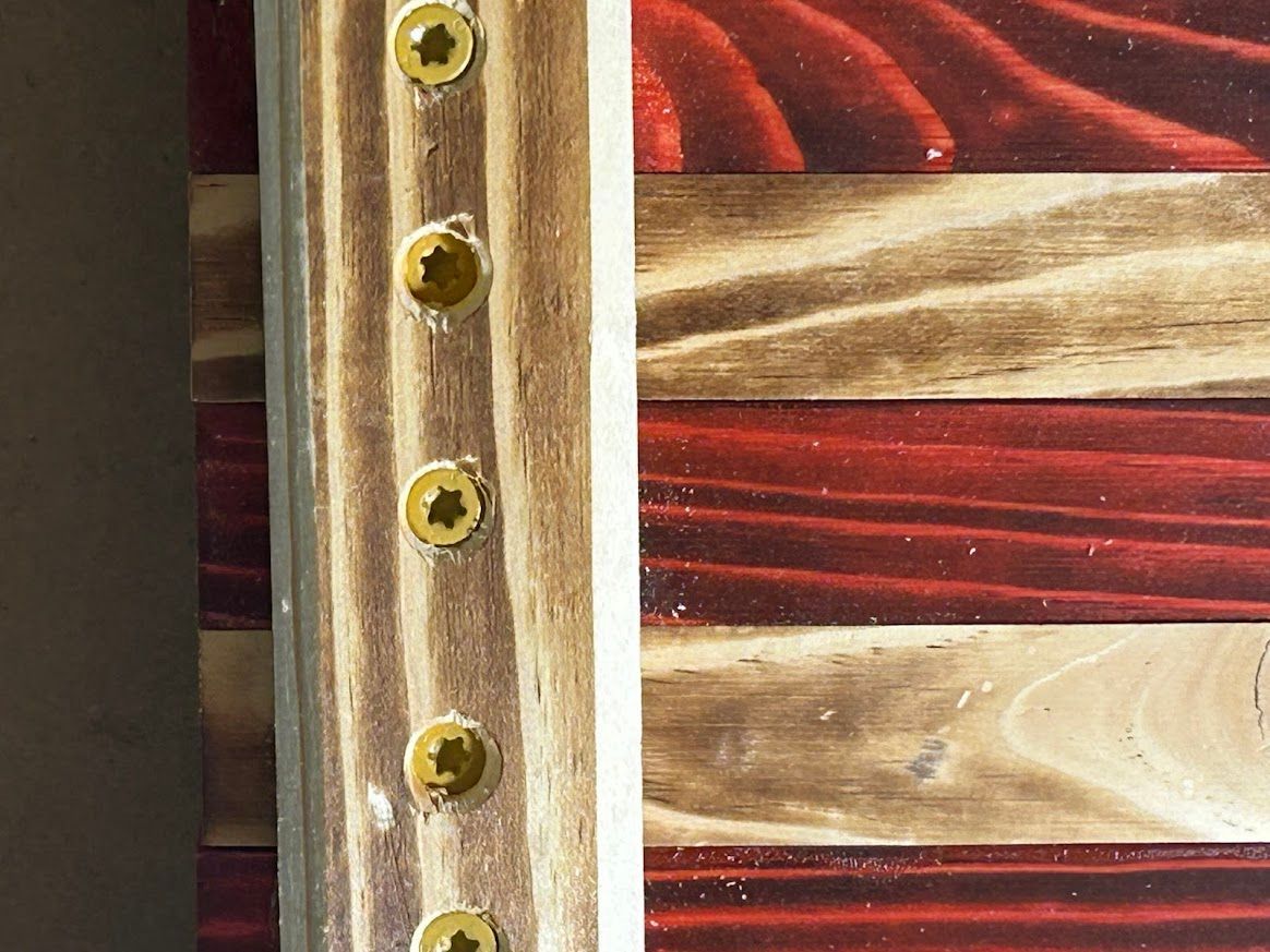 Wooden American flag, with vertical wooden strips and gold screws securing the frame.
