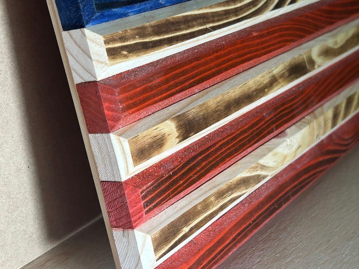 Wooden American flag with blue, red, and white stripes; side view showing burnt wood grain detail.