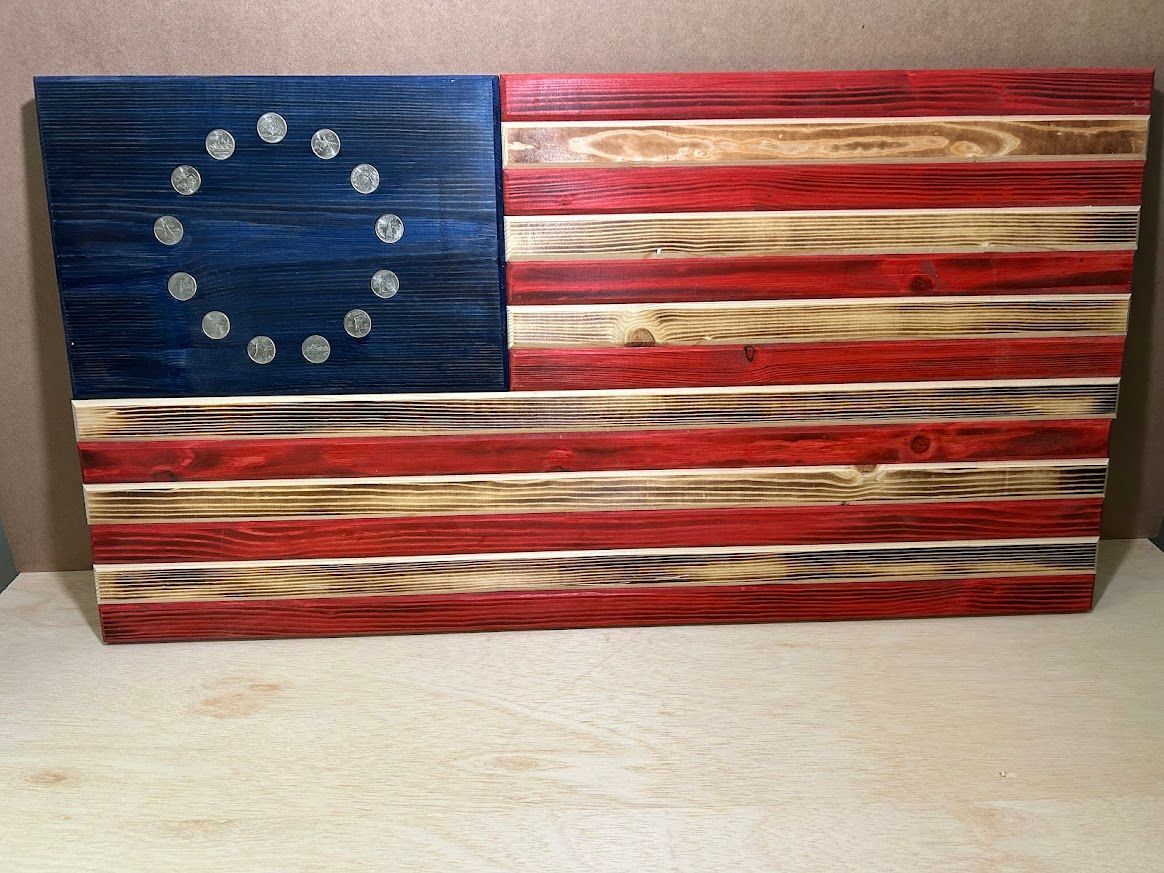 Wooden flag of the United States, blue field with 13 silver stars, red and white stripes, rustic appearance.