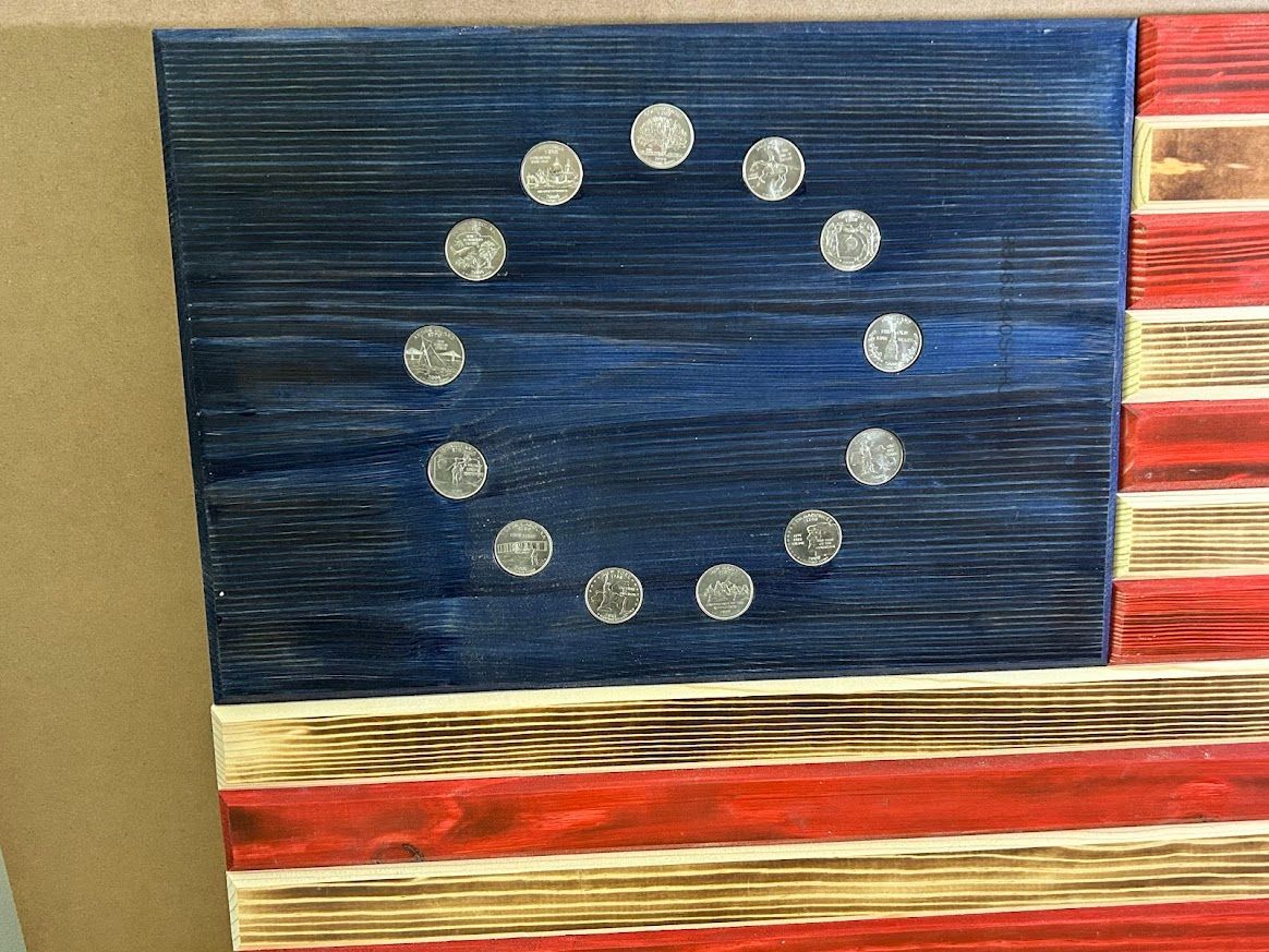 Wooden American flag with a circle of 13 silver coins on a blue field. Red and white stripes.