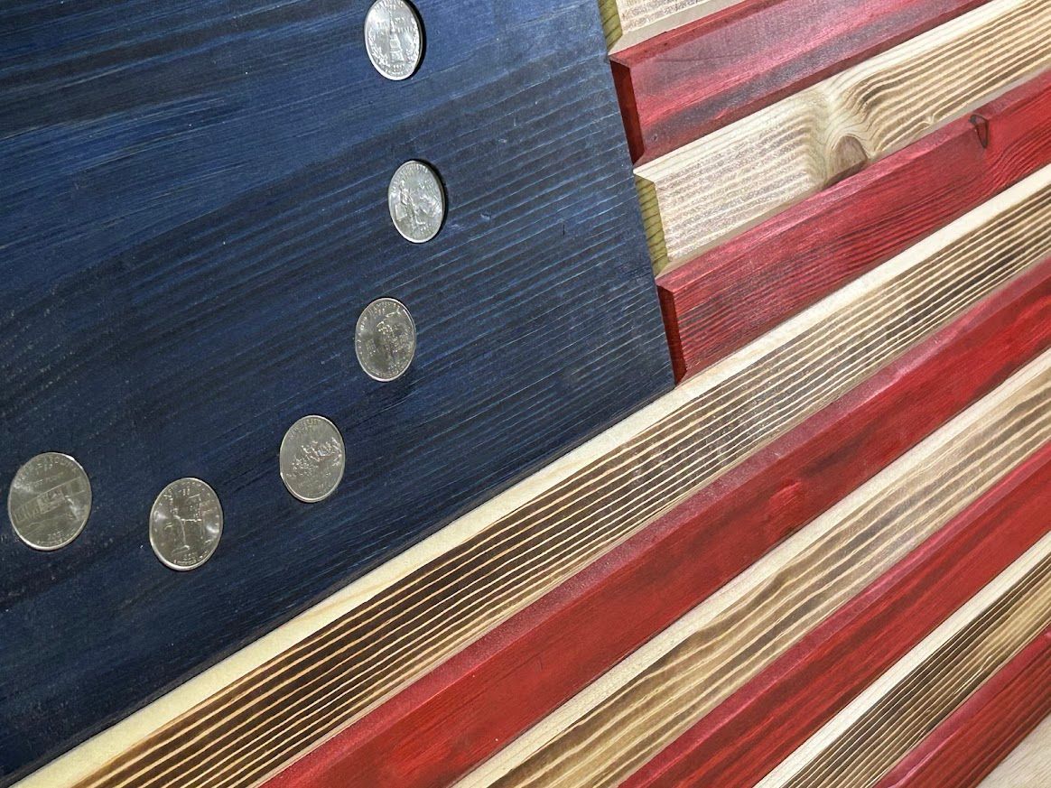 Wooden flag of the United States, blue field with 13 silver stars, red and white stripes, rustic appearance.