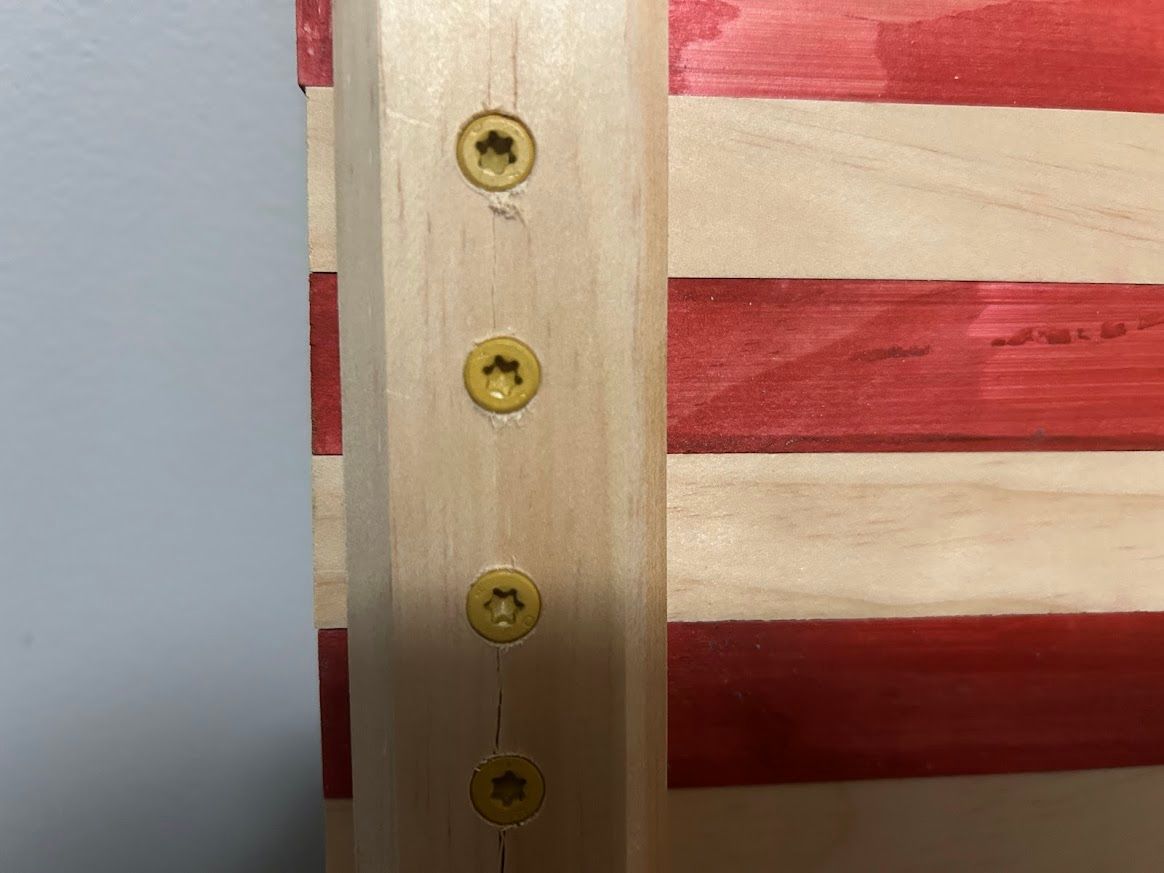 Wooden American flag with red and white stripes; a vertical wooden beam attached by yellow screws.
