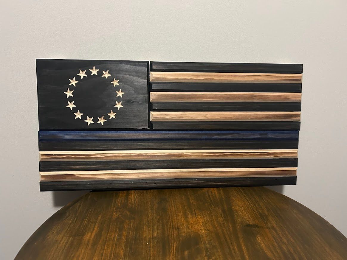 Wooden, rustic American flag art on a brown table. Features stars in a circle, black and tan stripes, and a blue line.