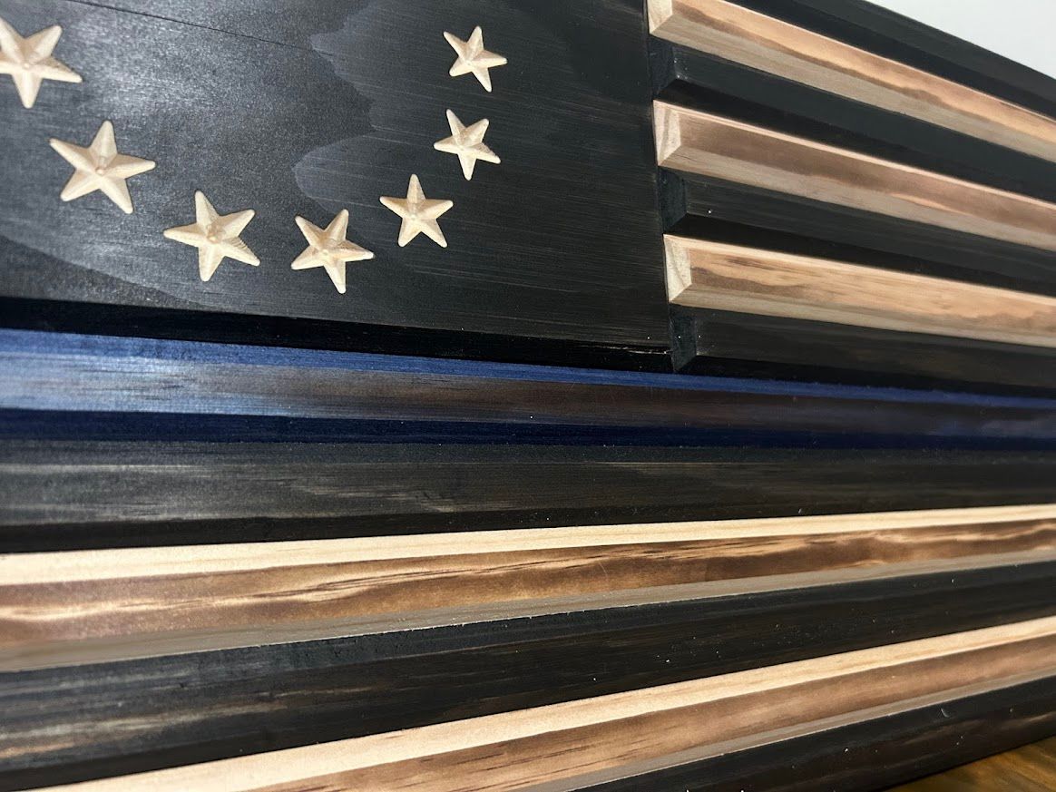 Wooden, rustic American flag art on a brown table. Features stars in a circle, black and tan stripes, and a blue line.