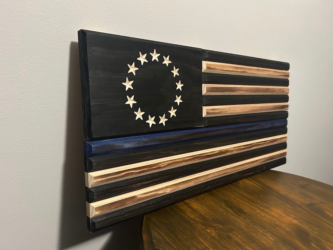 Wooden American flag with a blue line and 13 stars, displayed on a wall and table.