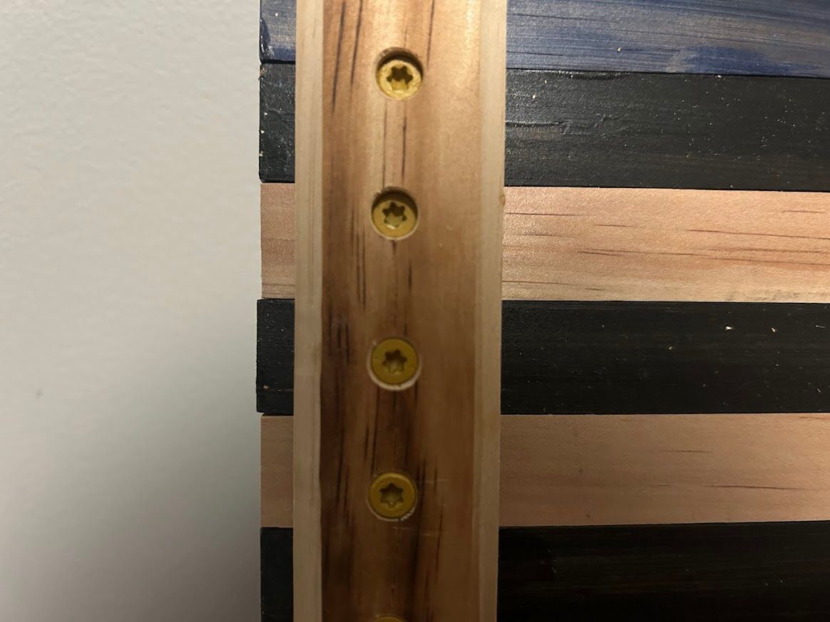 Close-up of a wooden flag, showing screws in a vertical wood support piece.