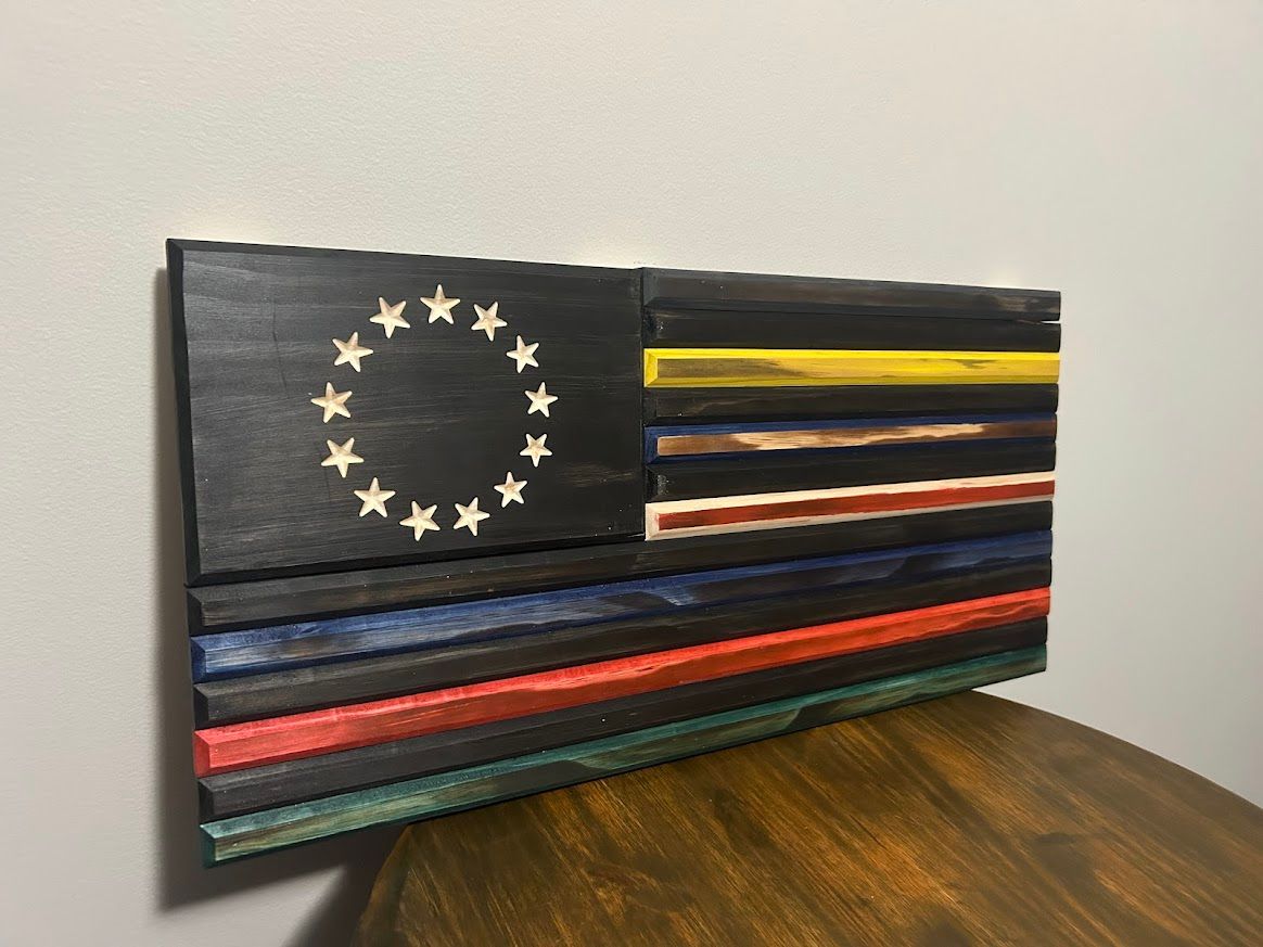 Wooden flag art with a black field of stars and horizontal stripes in various colors, including a yellow stripe.