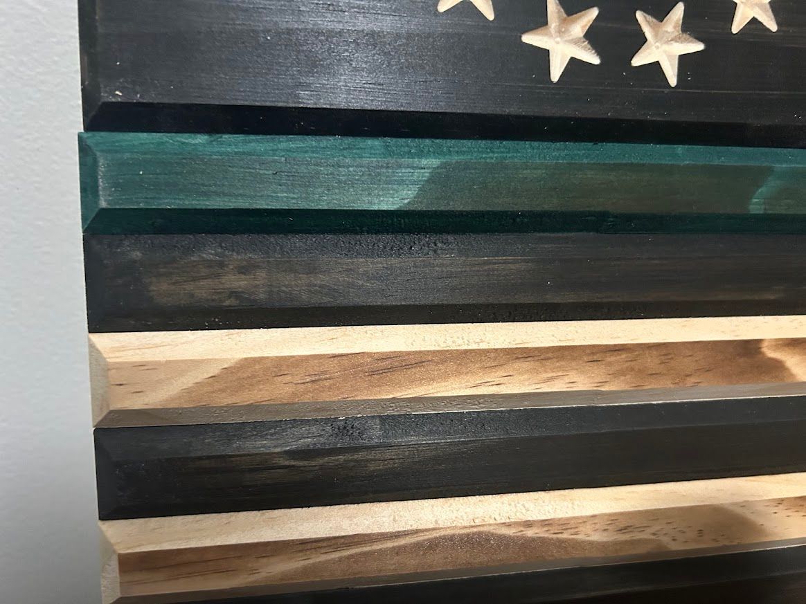 Wooden American flag carving with green stripe, stars, and black and natural wood stripes.