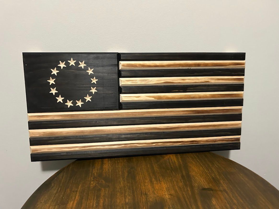 Wooden American flag, black and natural wood, 13 stars in a circle, hanging on a wall.