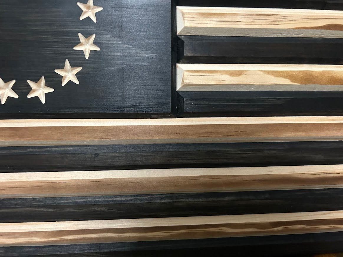 Wooden American flag, black and natural wood, 13 stars in a circle, hanging on a wall.