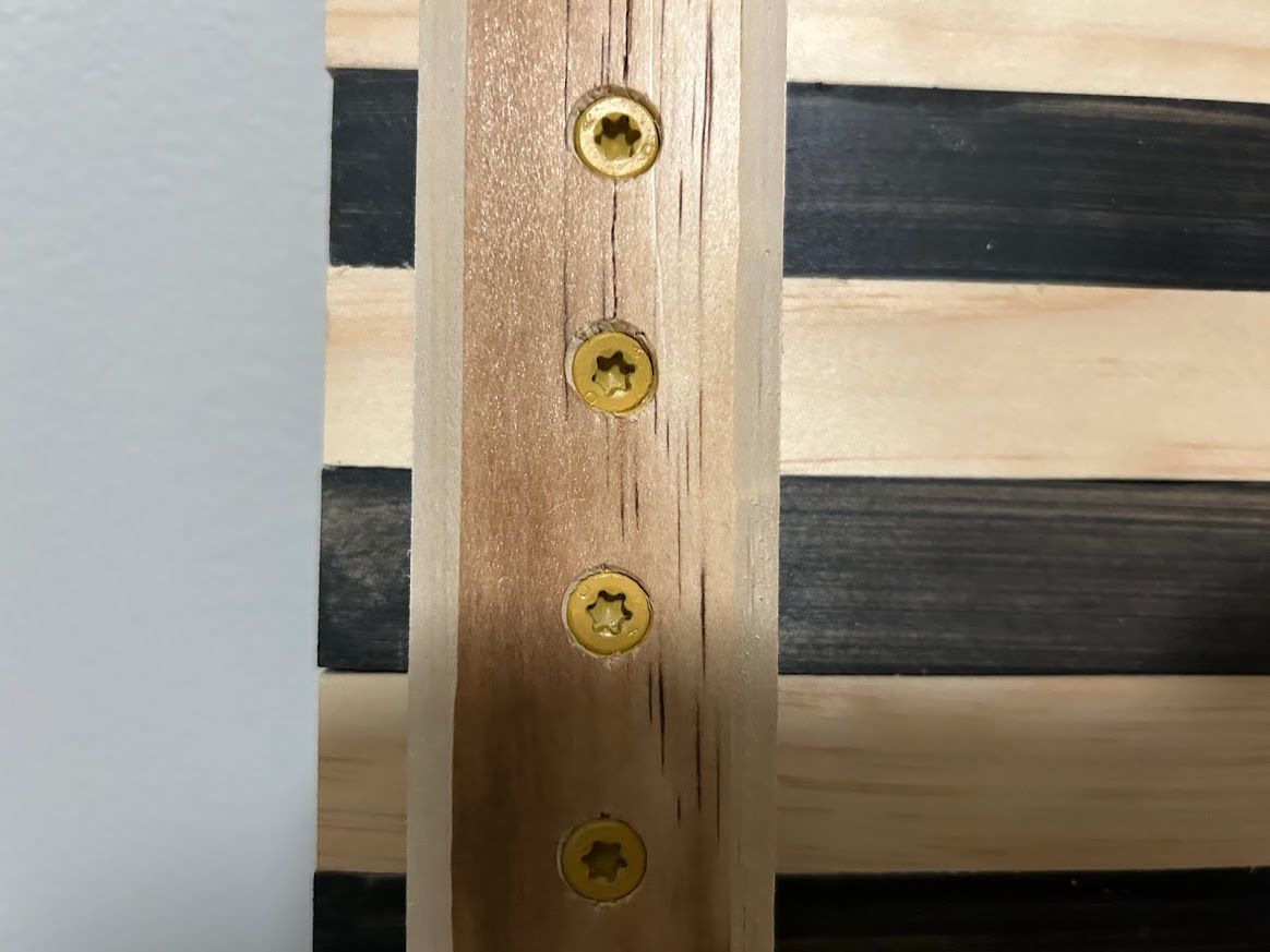 Close-up of wooden American flag with support beams attached by gold screws.