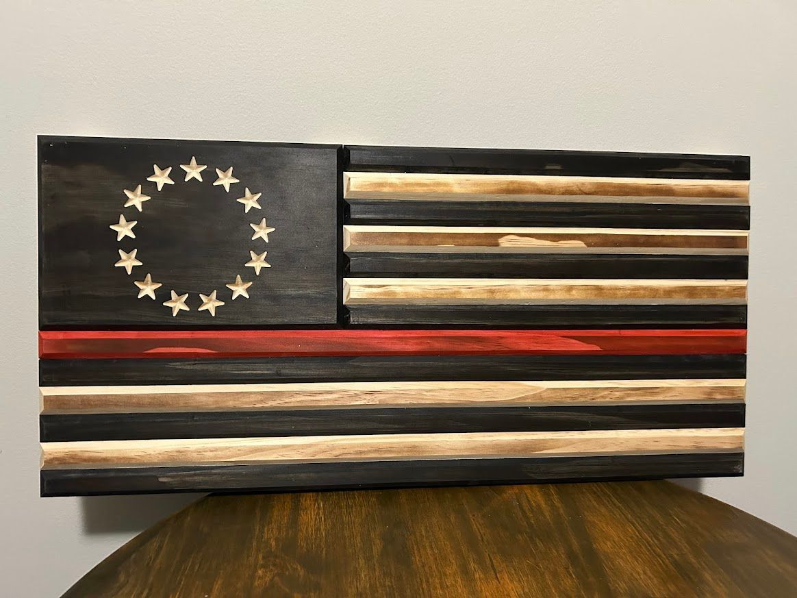 Wooden flag art with black, natural wood, and a red line. The flag has a circle of stars.