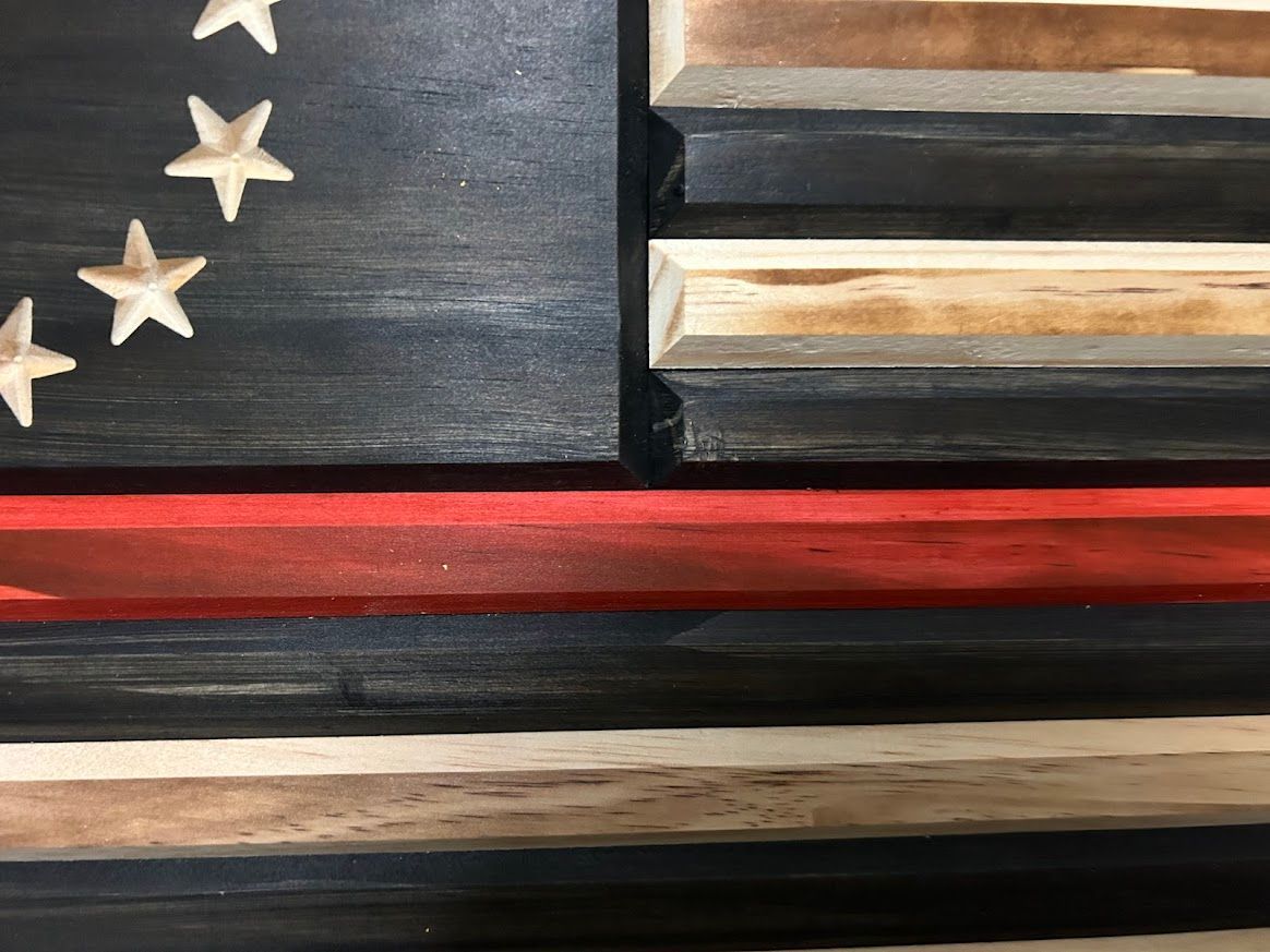 Wooden flag art with black, natural wood, and a red line. The flag has a circle of stars.