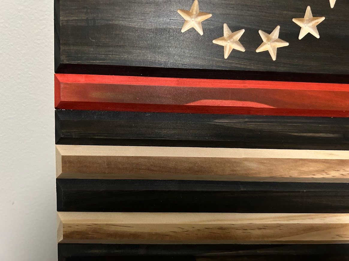 Wooden flag with carved stars, black stripes, and a red line.