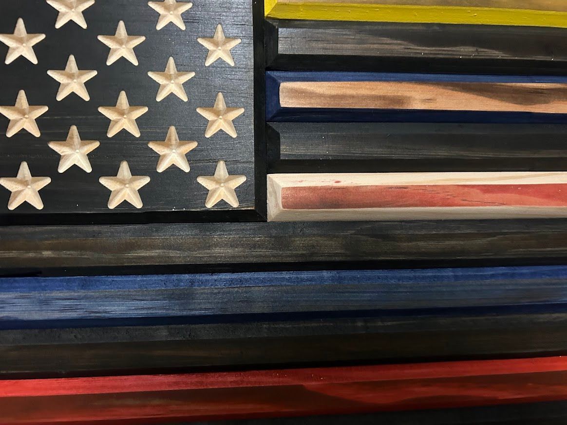 Wooden American flag with carved stars, black, yellow, blue, red, green stripes.