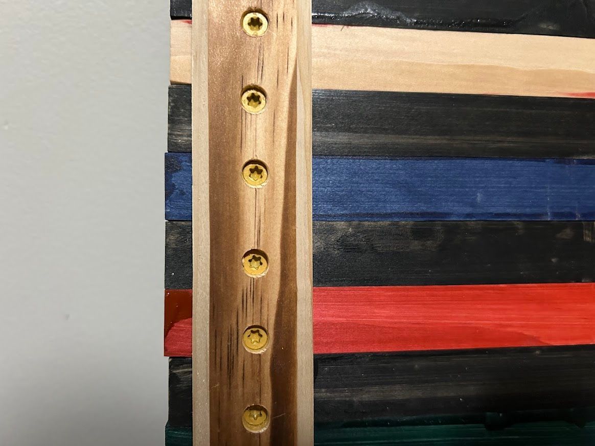 Wooden artwork with horizontal painted stripes, secured with a vertical wooden strip and brass screws.