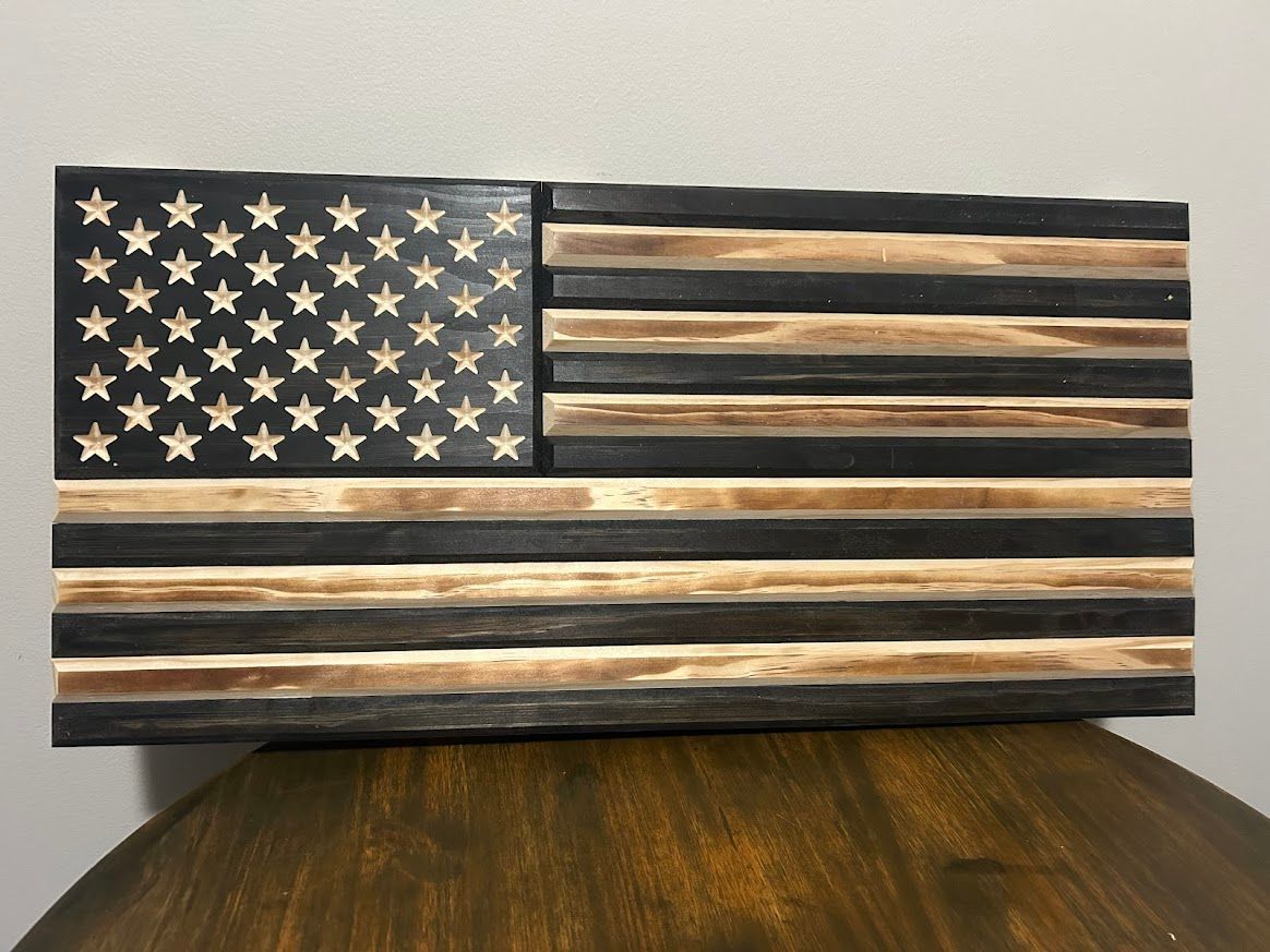 Wooden American flag with carved stars, black and tan stripes, on a wooden surface.