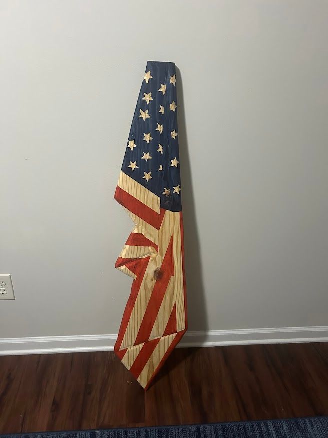 Wooden American flag art piece leaning against a gray wall.