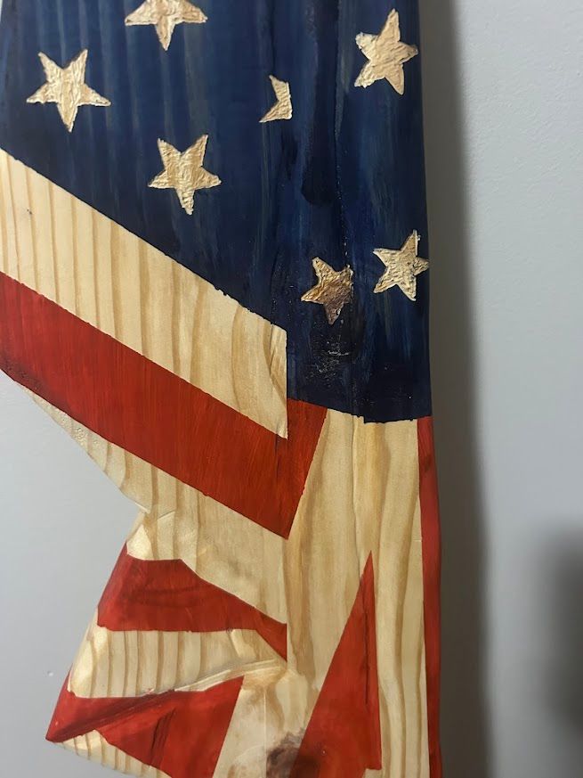 Wooden American flag art piece leaning against a gray wall.