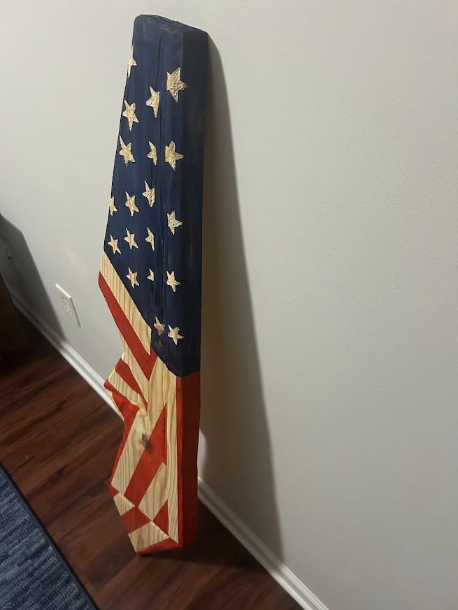 Wooden carved American flag, leaning against a white wall.