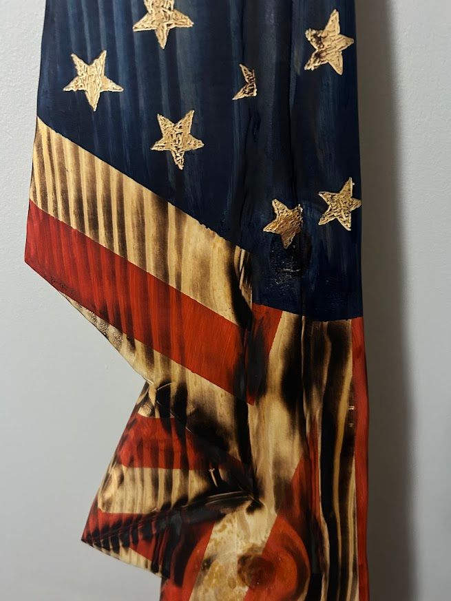 American flag wall hanging, folded, against a light gray wall and dark wood floor.