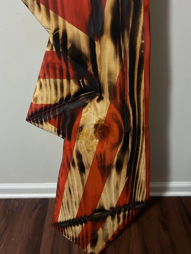 Red and white striped, charred wood flag art, mounted on a wall.
