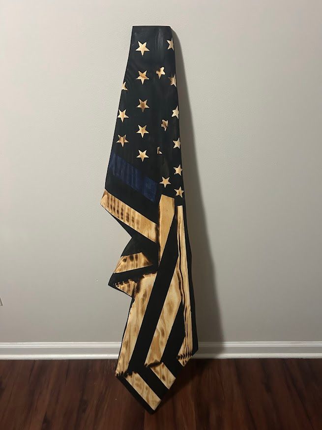 Wooden American flag, black and natural wood, with blue stripe, mounted on a wall.