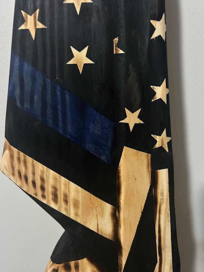 Wooden American flag, black and natural wood, with blue stripe, mounted on a wall.