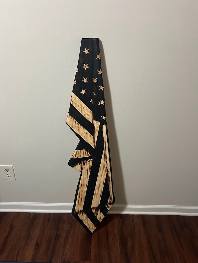 Wooden American flag hanging on a gray wall with a wood floor.