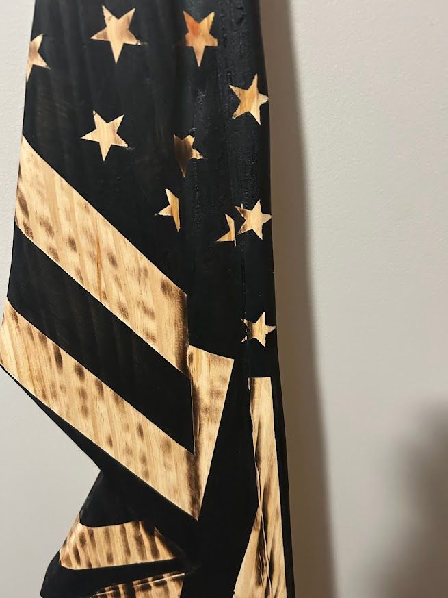 Wooden American flag hanging on a gray wall with a wood floor.