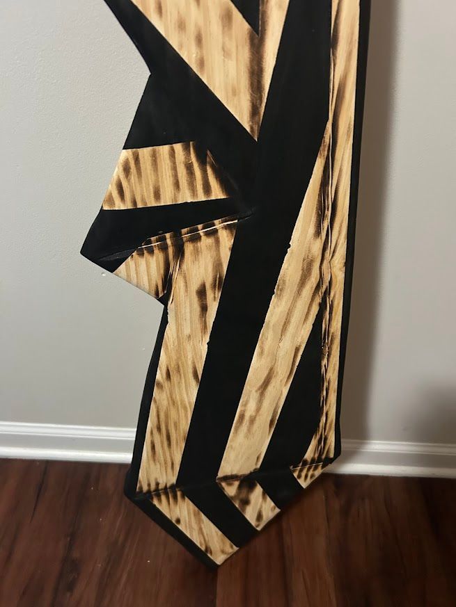 Wooden wall art with a black geometric design on a light brown background.