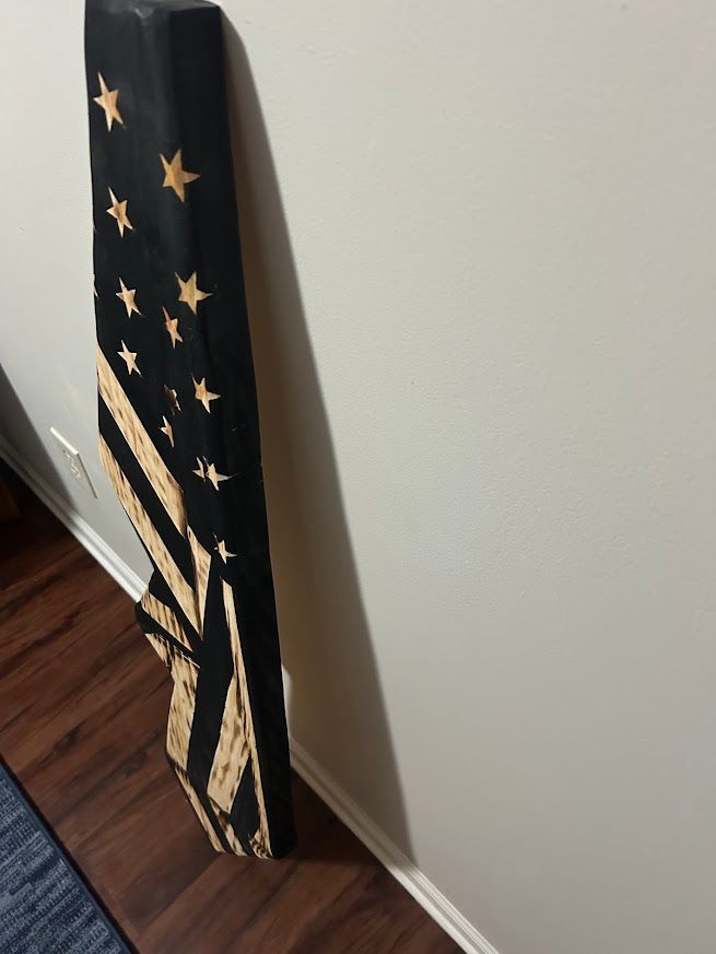 Wooden American flag leaning against a white wall. Stars and stripes are visible.