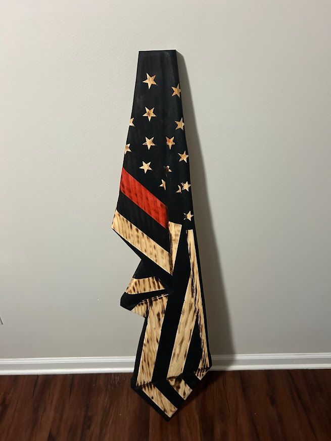 American flag with red line, leaning against a gray wall on wood floor. Black field with stars, tan stripes.