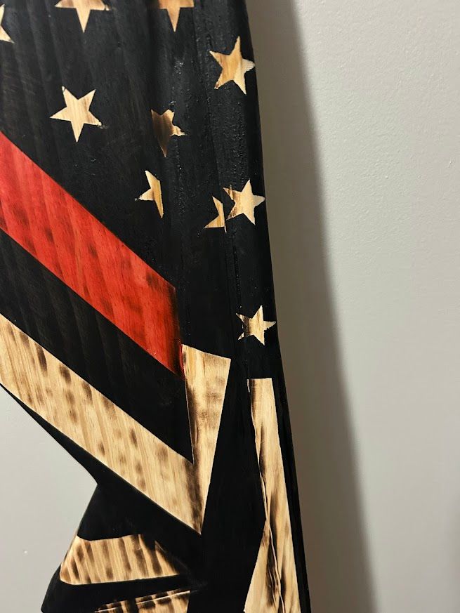 American flag with red line, leaning against a gray wall on wood floor. Black field with stars, tan stripes.