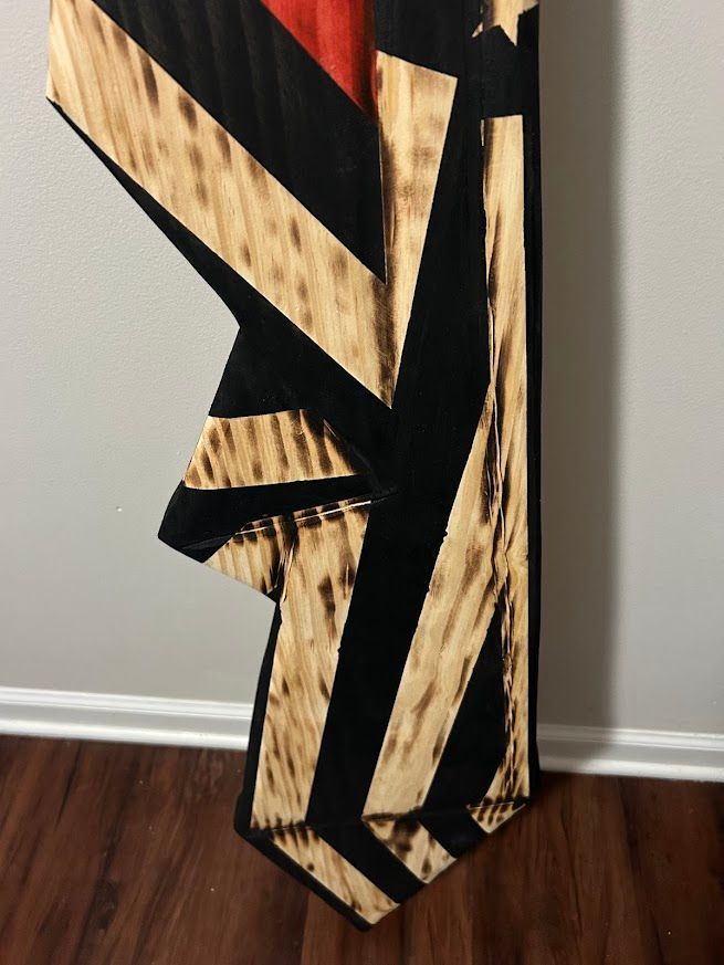 Wooden, charred flag art; black stripes on wood; red stripe at top; star visible.