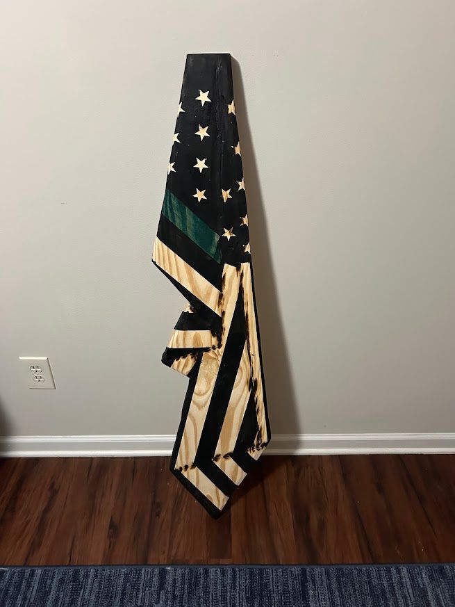 Black, green, and tan wooden flag hanging on a gray wall.