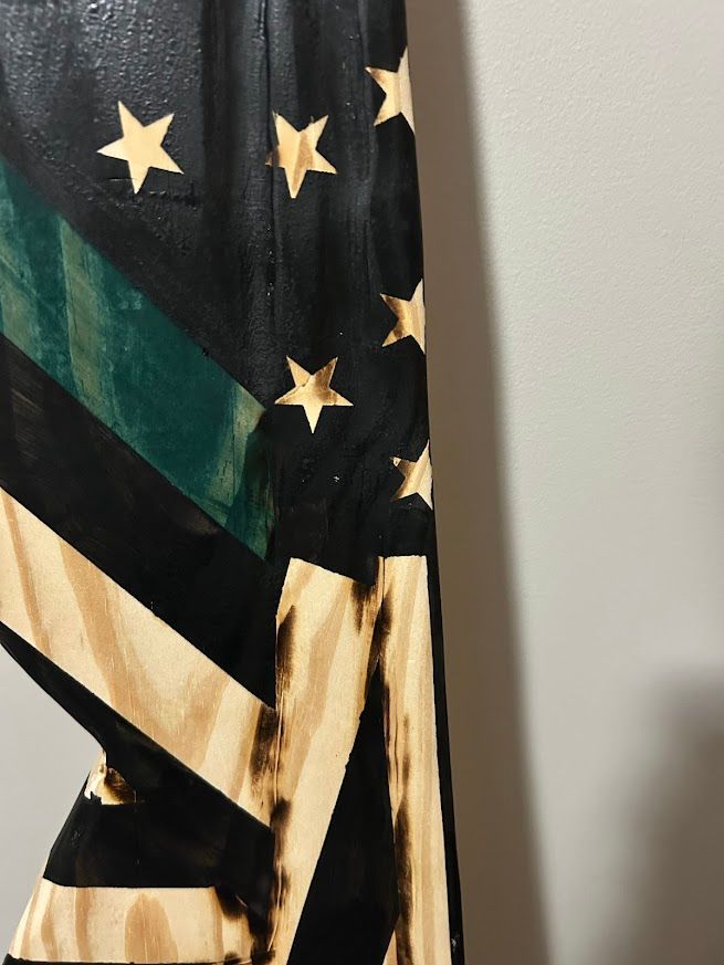 Black, green, and tan wooden flag hanging on a gray wall.