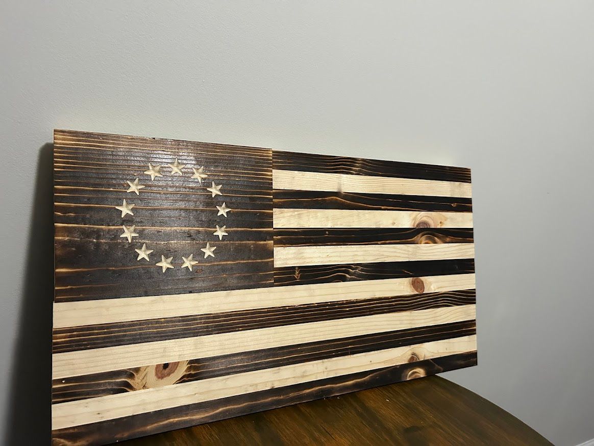 Wooden Betsy Ross flag, dark brown stained with light wood stripes, on a wood surface.
