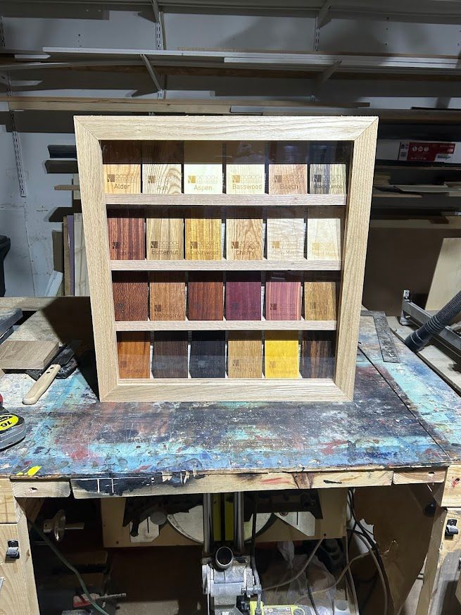 Wooden display case holding various wood samples on a workbench.